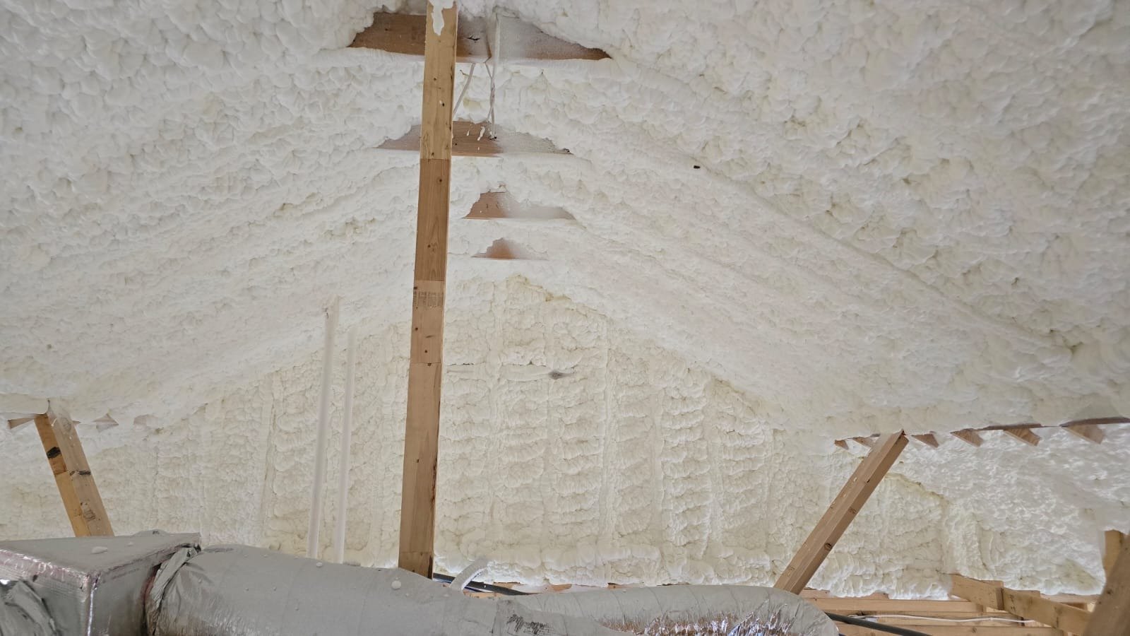 Spray foam insulation being applied to an attic roofline mid-installation, showing raw unfinished trim edges against wood framing
